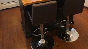 Een keuken met groene kastjes, een houten kookeiland met twee zwarte barkrukken, een kroonluchter en moderne apparaten.