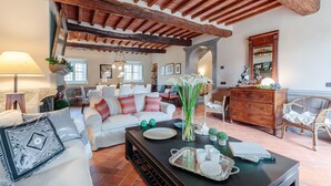 A spacious living room with a high wooden ceiling, a white sofa, a dining area, and a wooden dresser. - Villa BRUNETTA, Discover your Modern but Traditional Villa in Lucca (Capannori)