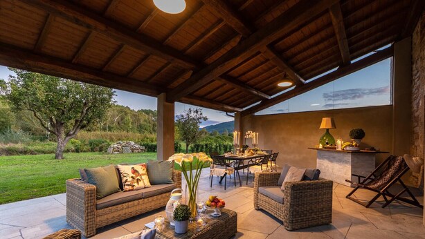 An outdoor patio with wicker furniture, a dining table set for four, and a view of the countryside. - Villa BRUNETTA, Discover your Modern but Traditional Villa in Lucca (Capannori)