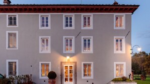 A multi-story building with a symmetrical facade, evenly spaced windows, and a central entrance with a door and glass panels. - Villa BRUNETTA, Discover your Modern but Traditional Villa in Lucca (Capannori)