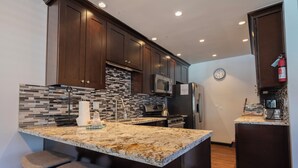 A modern kitchen with dark wood cabinets, a tiled backsplash, granite countertops, stainless steel appliances, and a clock on the wall. - Edgewater #20 - 2 BD/2 BTH (June Lake)