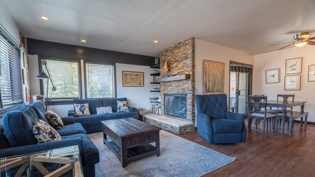 A modern living room with a stone fireplace, a blue sofa, a dining table, and a ceiling fan. - Edgewater #20 - 2 BD/2 BTH (June Lake)
