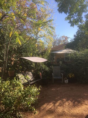 A garden area with a swing chair, a table, and an umbrella. There are potted plants and a brick building in the background.