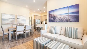 A modern living room with a sofa, ottomans, and a dining area with chairs and a table.