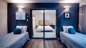 Habitación de hotel con dos camas, una amplia puerta corredera que da al baño y luces fijadas a la pared.
