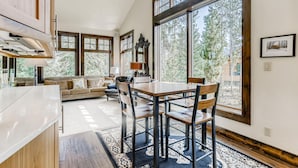 A modern kitchen with a dining area, large windows, and a view of trees. - Wellington Haus: Dog Friendly Home, Hot Tub, Views (Breckenridge)