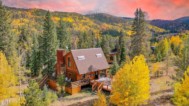 A cabin with a deck and a covered porch, surrounded by a forest with autumn foliage. - Wellington Haus: Dog Friendly Home, Hot Tub, Views (Breckenridge)