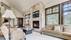 A spacious living room with a stone fireplace, large windows, and a cozy seating area. - Wellington Haus: Dog Friendly Home, Hot Tub, Views (Breckenridge)