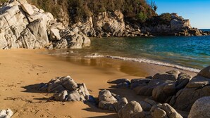 A rocky beach with clear water, surrounded by large boulders and sparse vegetation. - Gated Ocean View Villa with Direct Beach Access (Huatulco)