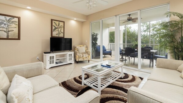 Una sala de estar con televisor, sofá, mesa de centro y puerta corrediza de vidrio que da a un patio exterior.