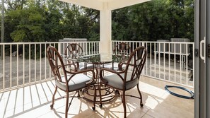 Un patio cubierto al aire libre con una mesa de vidrio y cuatro sillas, rodeado por una barandilla blanca.
