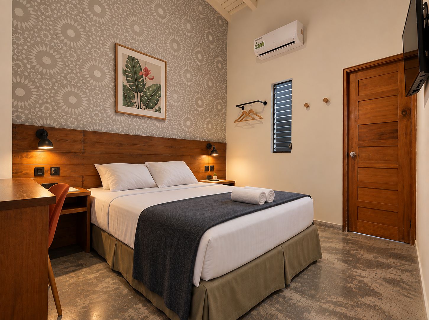 A bedroom with a bed, bedside tables, a desk, a chair, a hanging coat rack, and a door.
