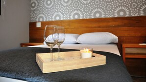 A neatly made bed with a wooden headboard, a bedside table with a lamp, and a tray with two glasses and a candle. - Canova (Panama City)