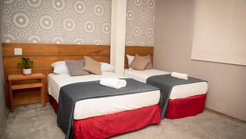 Une chambre avec deux lits, chacun recouvert d’une couvre-lit grise et rouge, dotés d’une tête de lit en bois et d’une table de chevet sur laquelle est posée une plante.