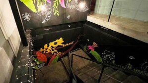 A modern interior with a black wall featuring colorful leaf and flower designs, a glass table with a frog decoration, and a staircase leading to a higher level. - Canova (Panama City)