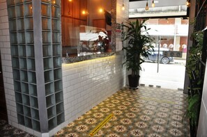 A reception area with a tiled floor, a potted plant, and a window with a view of the street. - Canova (Panama City)