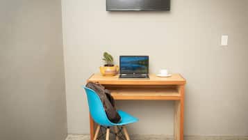 Un pequeño espacio de trabajo con una computadora portátil, una taza y una planta sobre un escritorio de madera frente a una pared lisa.