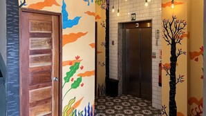 A hallway with a wooden door, an elevator, and walls decorated with colorful murals. - Canova (Panama City)