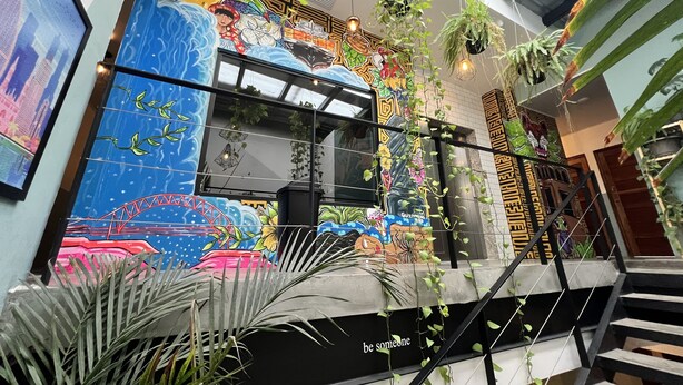 A modern interior with a colorful mural, hanging plants, and a staircase. - Canova (Panama City)