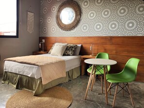 A bedroom with a bed, bedside table, lamp, and a round mirror on the wall. - Canova (Panama City)