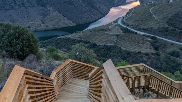 A wooden staircase leading to a terrace overlooking a river valley with terraced fields.