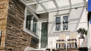A modern house with a stone facade, a glass conservatory, and a white staircase leading to a balcony with outdoor seating.