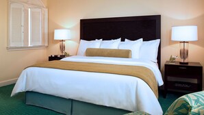 Een hotelkamer met een groot bed, twee nachtkastjes met lampen, een groen tapijt en een raam met shutters.