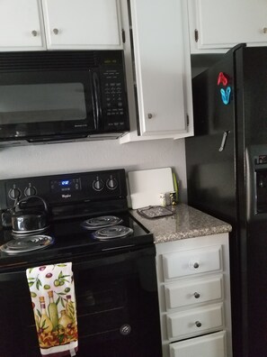 Une cuisine avec un micro-ondes noir, une cuisinière, un réfrigérateur et des armoires blanches.