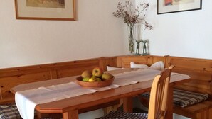 A wooden dining table with a white tablecloth, a bowl of fruit, and checkered cushions on chairs. - Ferienwohnung, 55 qm Obergeschoss, 1 Separates Schlafzimmer (Bad Endorf)