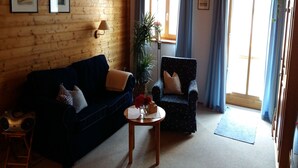A cozy living room with a dark blue sofa, a patterned armchair, and a small round table with a vase of flowers. - Ferienwohnung, 55 qm Obergeschoss, 1 Separates Schlafzimmer (Bad Endorf)