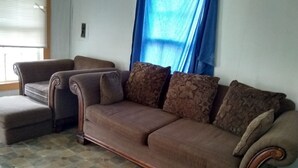 A living room with a brown sofa set, patterned cushions, and a tiled floor.