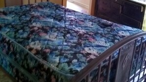 A bedroom with a bed, a wooden headboard, a dresser, and a door leading to another room.