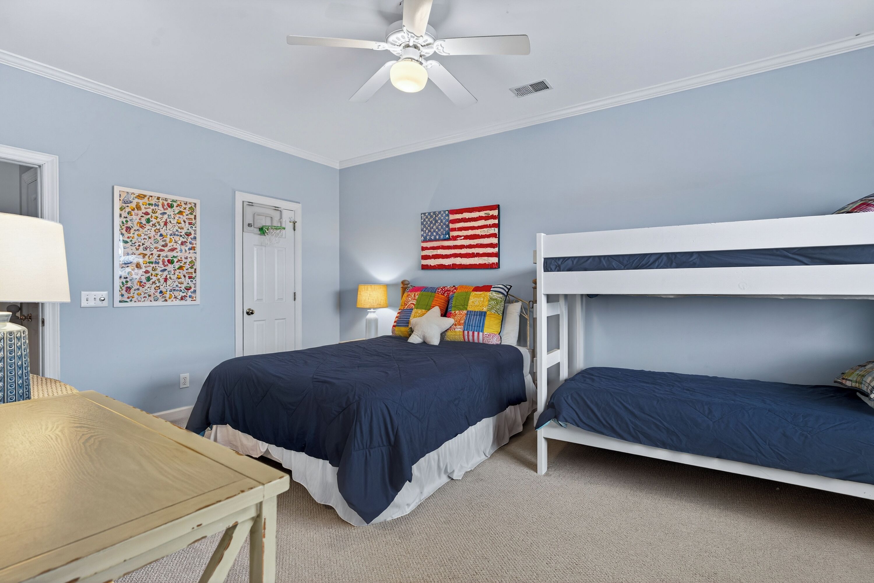 A bedroom with a single bed, a bunk bed, a ceiling fan, a door, and a wall with an American flag.