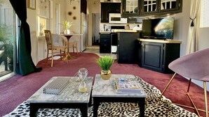 Ein Wohnzimmer mit einem Leopardenmuster-Teppich, zwei Tischen mit Dekoration, einem Fernseher und einer Küchenzeile mit Schränken und Geräten.