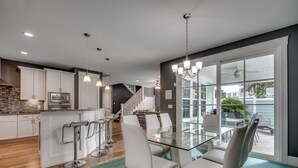 Een moderne keuken met een centraal eiland, barkrukken en een eethoek met een glazen tafel en stoelen.