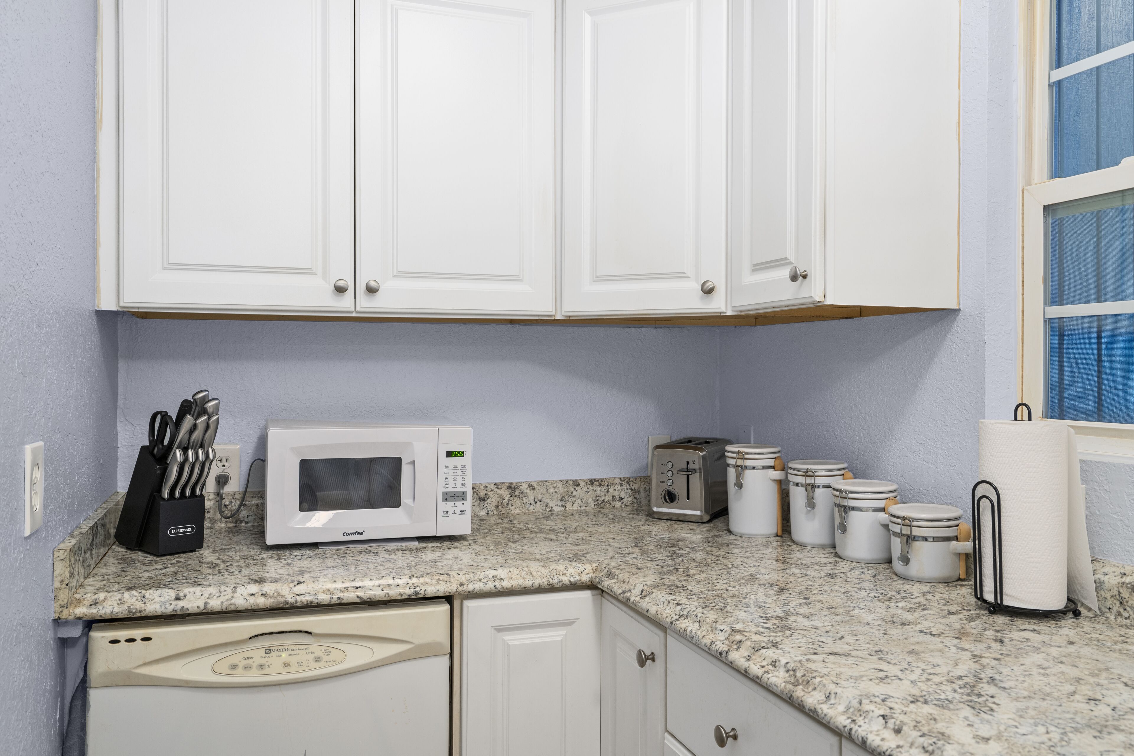 A kitchen with white cabinets, a microwave, toaster, and storage jars on the counter.