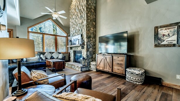 Una sala de estar acogedora con chimenea de piedra, un televisor de pantalla plana grande y un área de descanso confortable con sofás y otomanas de cuero.