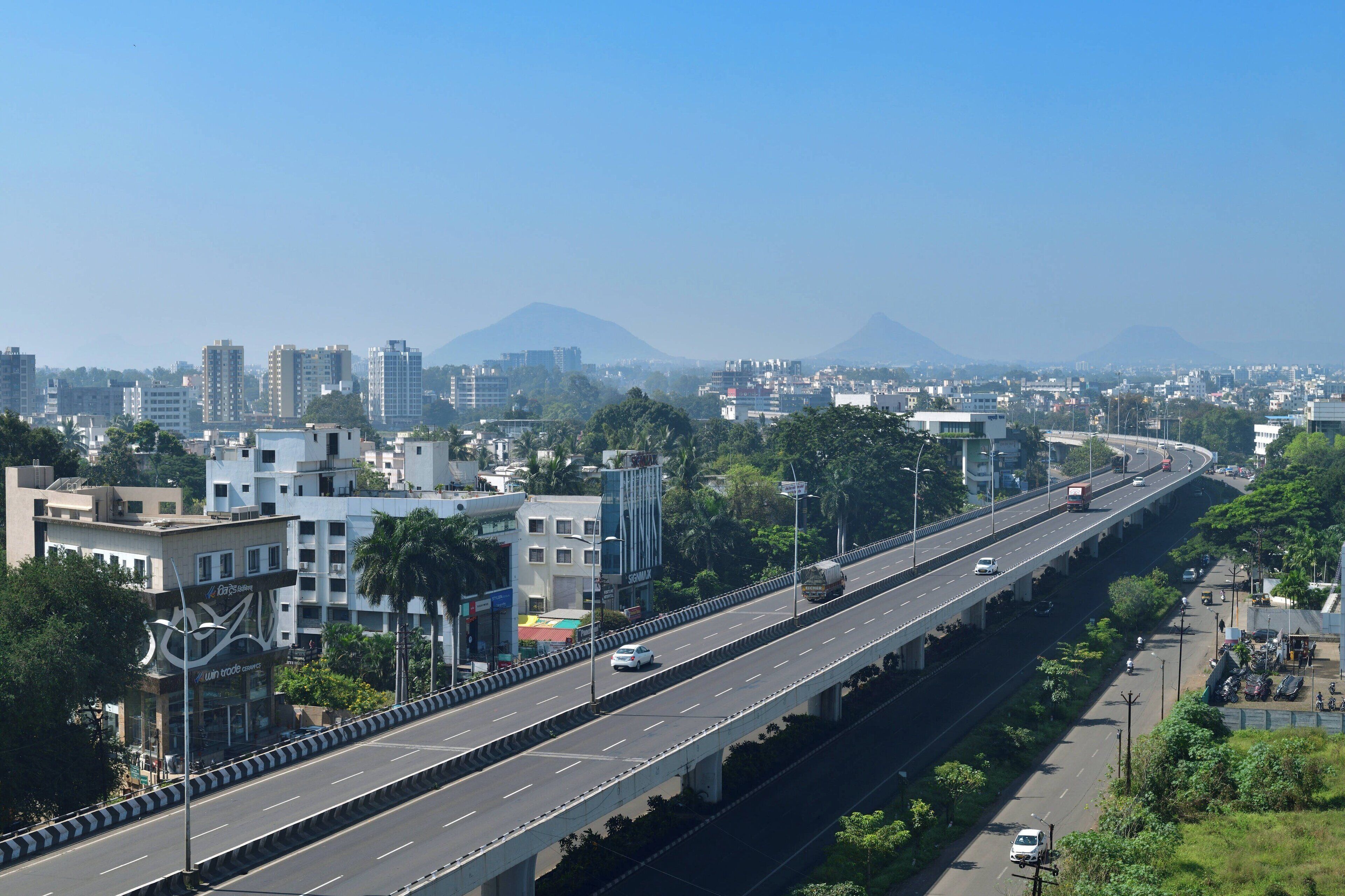 A multi-level highway with vehicles, urban buildings, and greenery.
