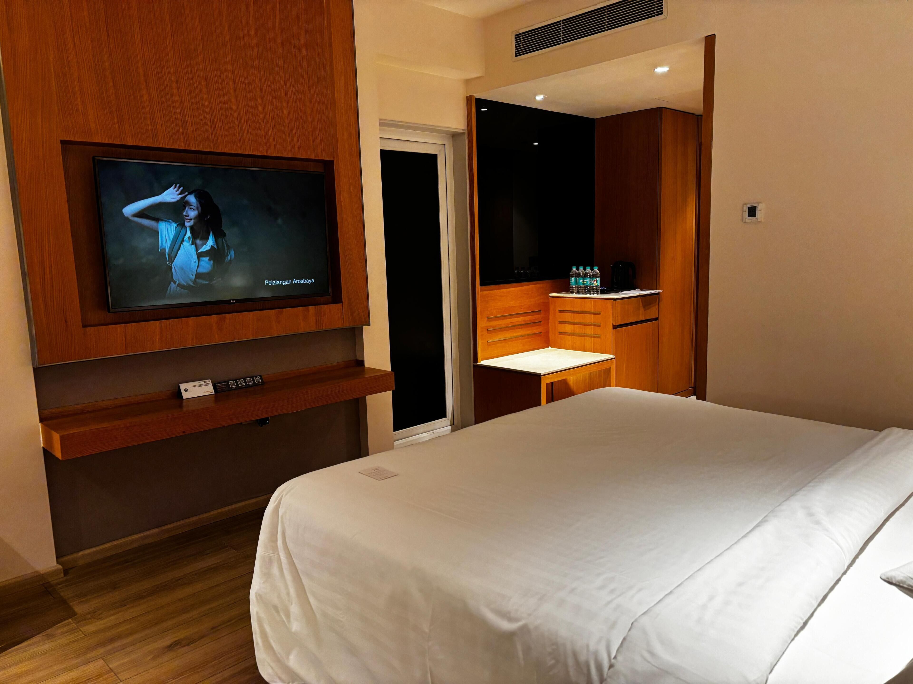 Habitación de hotel con cama, televisión montada en la pared, una mesita con silla y un minibar.
