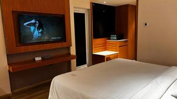 Habitación de hotel con cama, televisión montada en la pared, una mesita con silla y un minibar.