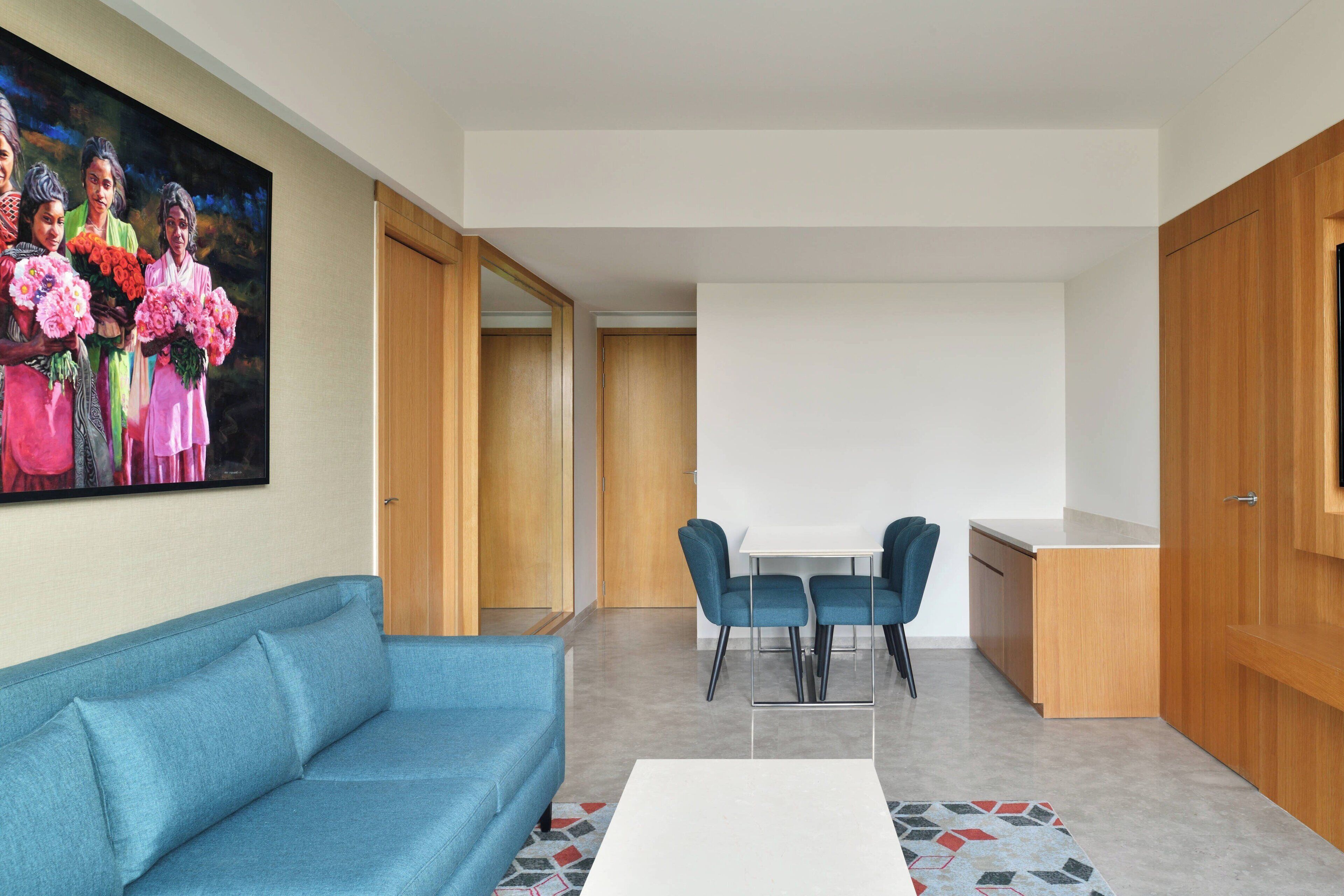 A modern living room with a blue sofa, a white coffee table, and a dining area with a white table and blue chairs.
