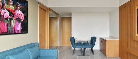 A modern living room with a blue sofa, a white coffee table, and a dining area with a white table and blue chairs.