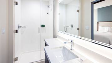 A modern bathroom with a glass-enclosed shower, a large mirror, and a white sink.