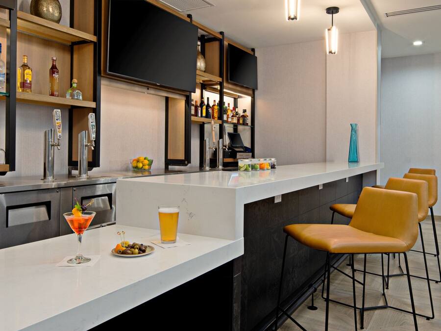 Een moderne bar met een lange toonbank, barstoelen en diverse flessen en glazen.