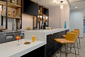 A modern bar area with a long counter, bar stools, and a variety of bottles and glasses.