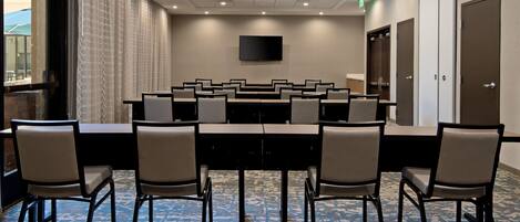 A conference room with a long table, multiple chairs, a flat-screen TV, and a patterned carpet.