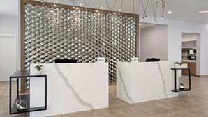 En reception med marmor bordplader, et geometrisk vægdesign og et fiskebensparket trægulv.