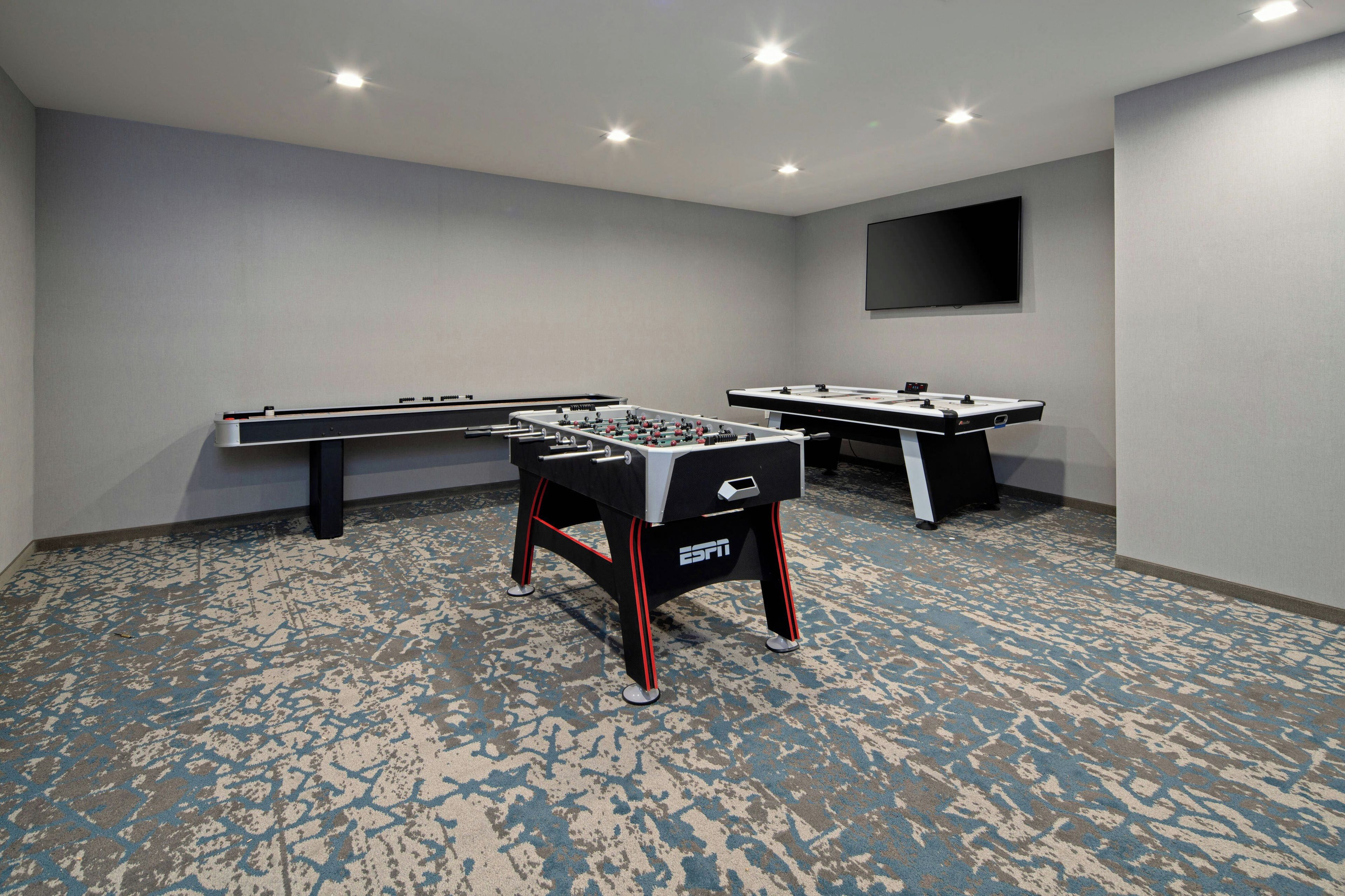 A room with two foosball tables and a flat-screen TV mounted on the wall.