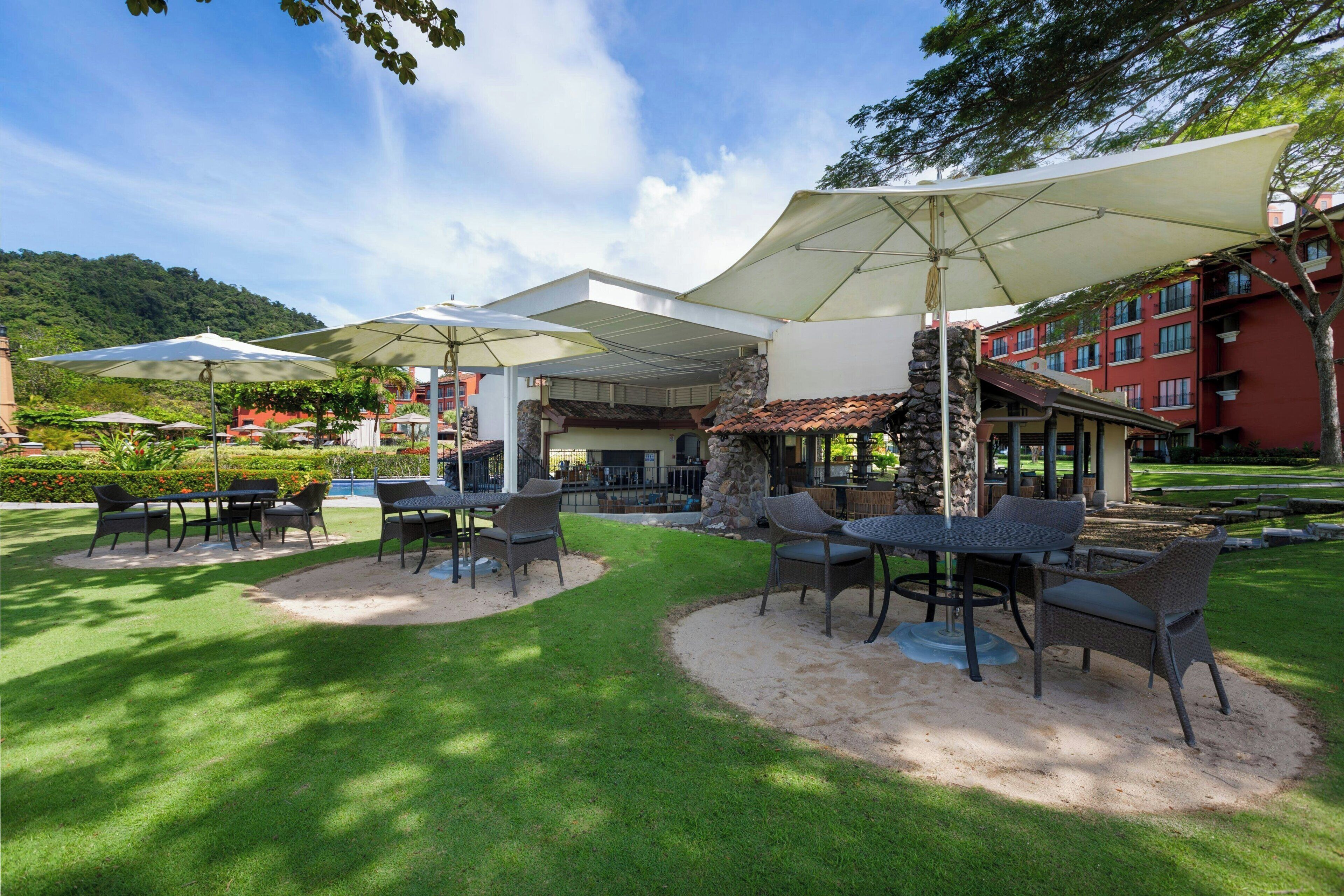 An outdoor patio with tables and chairs, umbrellas, and a stone structure.