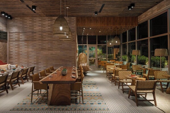 A spacious dining area with a long wooden table and multiple chairs, surrounded by large windows and natural light.
